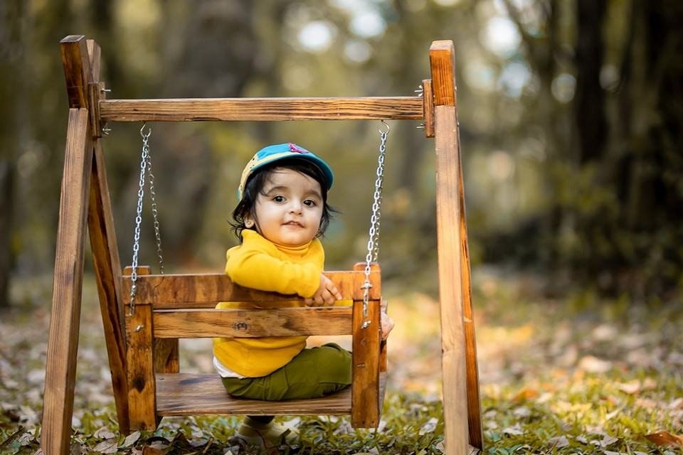 Smiling child wearing a cap seated on a small wooden swing and looking back for a playful portrait
