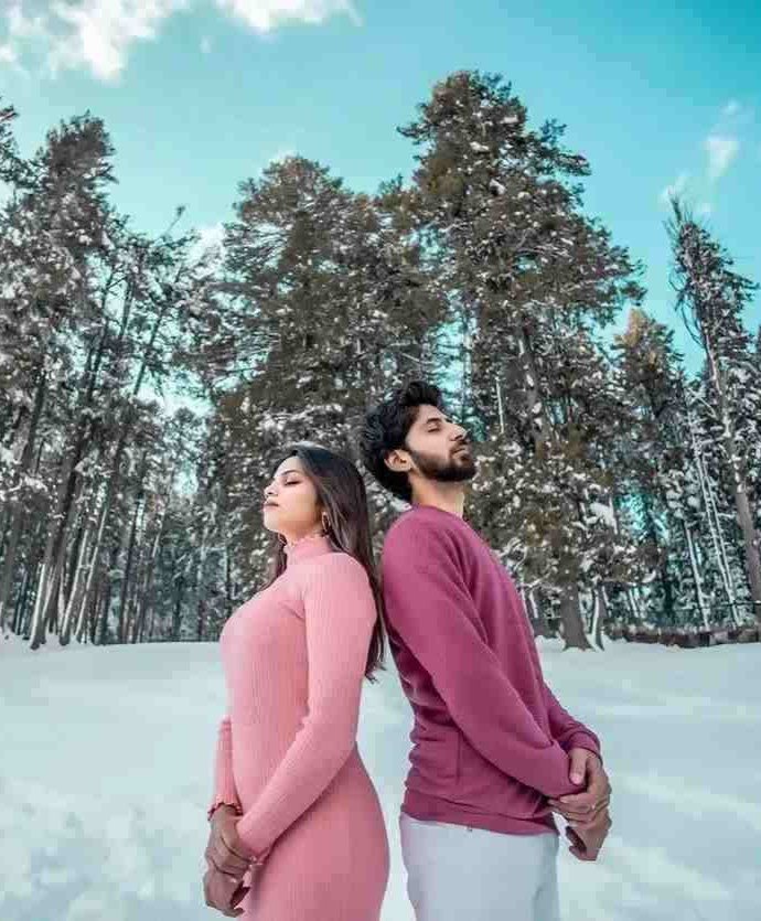 Couple standing back-to-back during a snowy pre-wedding shoot in a pine forest