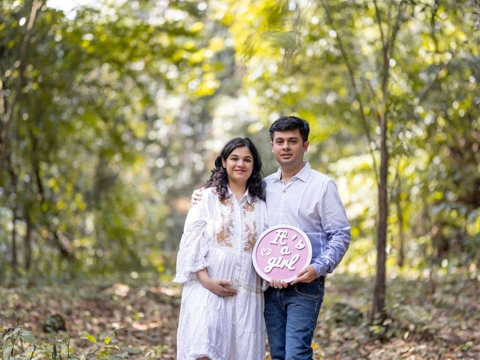 Happy expecting couple holding an “It’s a Girl” sign during an outdoor maternity photoshoot
